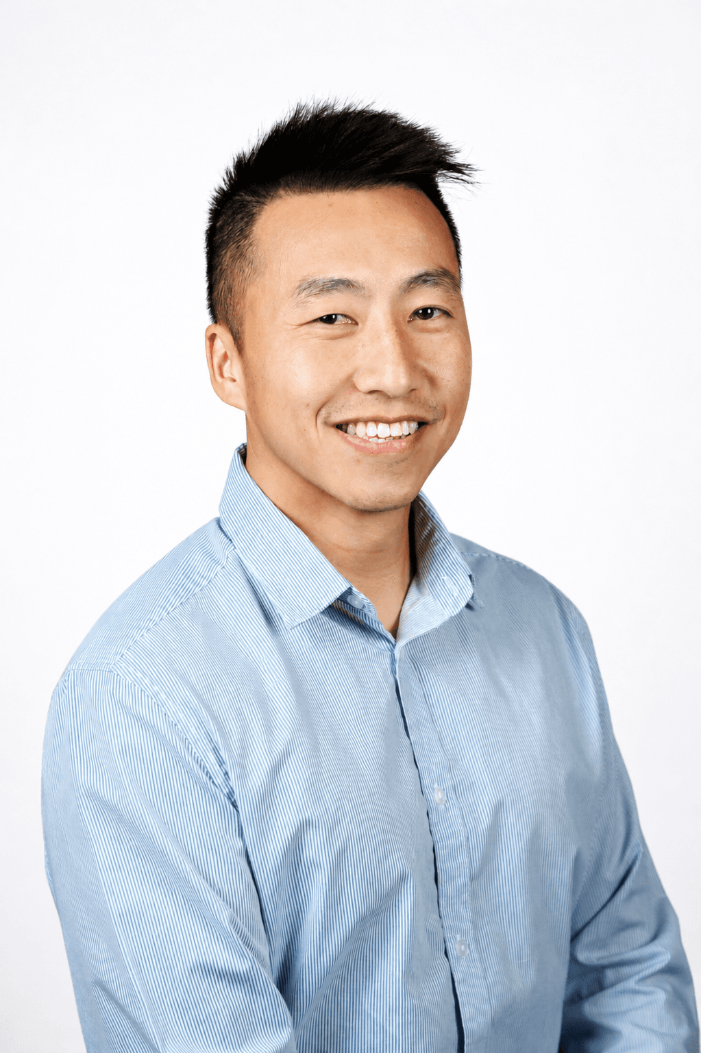 Smiling Asian man with short black hair wearing a light blue striped collared shirt.